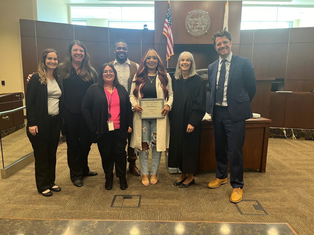 Image depicts Esther Bibriesca (center) surrounded by her support team with the Mental Health Diversion Court.