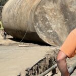 Image depicts an underground gas storage tank that has been placed above ground on the ground. Pipes are visible also.
