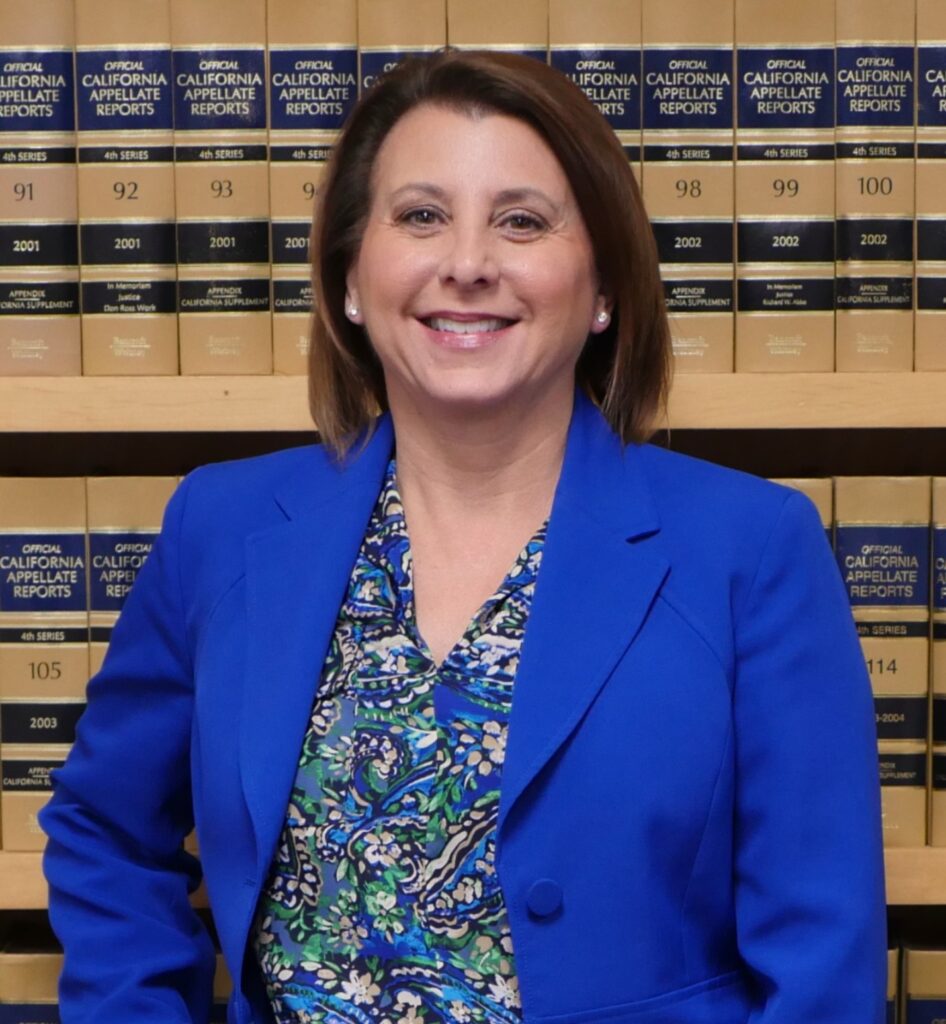 Image depicts Melinda Aiello in a blue suit standing in front of law books.